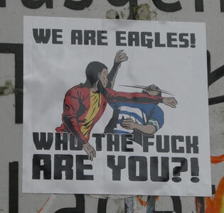 Sticker with drawing of someone in red sweater and yellow t-shirt punching someone in a blue and white t-shirt. Text: We are eagles! Who the fuck are you?!
