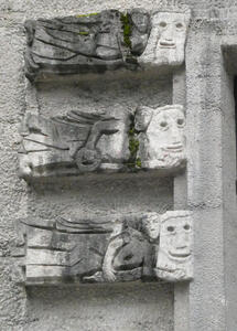 Three vertically stacked carvings of an angel carrying a large stone carved face.