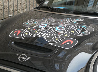 Hood of a black Mini Cooper with a decal in style of a mexican day-of-the-dead skull