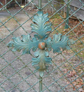 Decoration on a wire fence; it looks like four leaves at right angles to each other, joined at the stem with an orange button