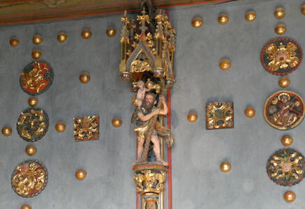 Colored statue of man holding a tree; child perched on shoulder. Around it, gold half-spheres on the wall