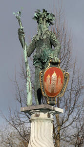 Statue of man with shaggy beard and leaf girdle, holding club in one hand and red-painted shield in other.