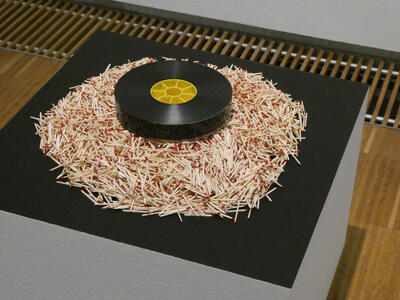 A spool of film with a yellow hub, surrounded by a pile of matchsticks.