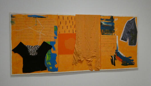 Large orange panel with articles of clothing attached to it, as well as some text written on the panel.