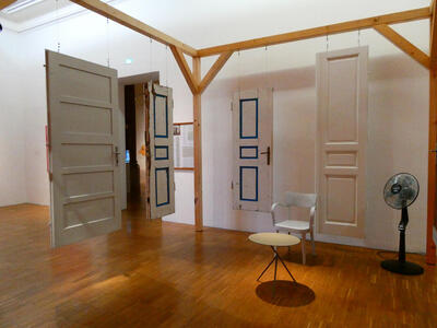 Four white wooden doors hanging from a wooden frame. Two of the doors have blue outline on the door panels.