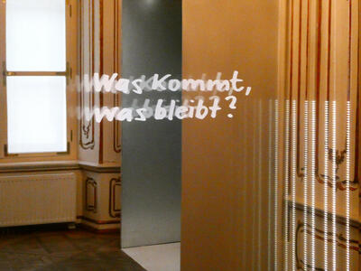 Glass panel with words written in white: „Was kommt, was bleibt?“