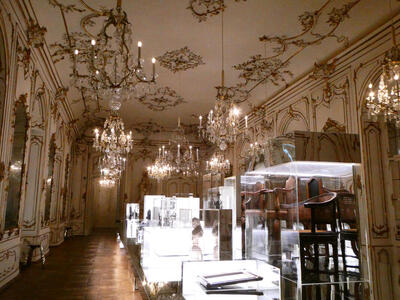 Large ballroom with many crystal chandeliers, gold patterns on ceiling, and display cases on floor.