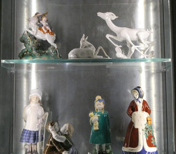 On top shelf, ceramic deer; on bottom, young girls and a woman in a shawl and hand muff