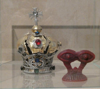 At left, a gold and silver crown with bue and red gemstones; at right, a red abstract sculpture that looks like a pair of eyes.
