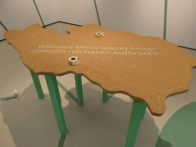 Wooden table map of austria with text „Welches Motiv steckt hinter deinem nächsten Aufbruch?“