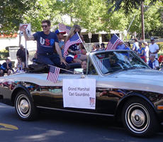 Man in blue T-shirt waving from rear seat of a convertible car