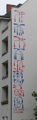 Abstract symbols in red and blue, painted vertically on buliding. At bottom: The world is a stage
