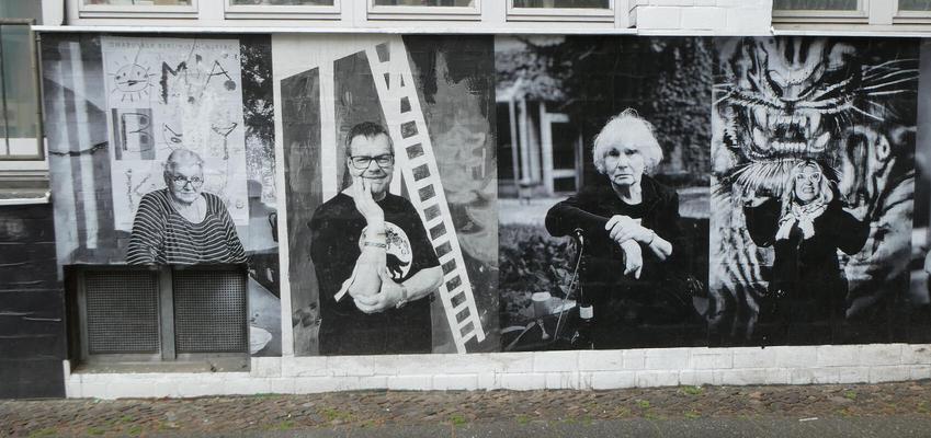 Black and white photos of four artists, looking at the camera. The last one has their hands on their temples and is shouting; in background is artwork of a lunging tiger.