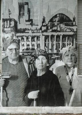 Three old ladies in headscarf carrying mops/brooms.
