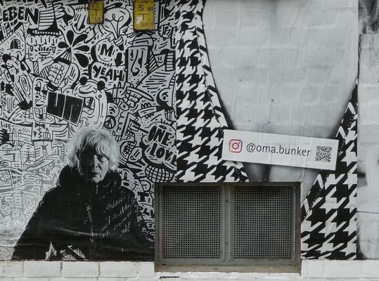 Woman in winter coat in front of graffitied wall. Instagram link to @oma.bunker at right