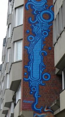 Abstract vaguely insect-like creature in blue on red brick vertical wall.