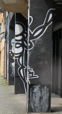Black and white abstract graffiti that is painted on two separate pillars. At the correct angle, it maes a continuous drawing.