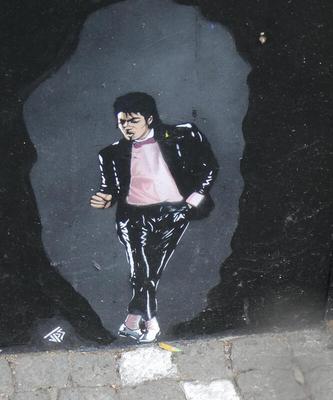 Michael Jackson in black jacket and pink shirt, doing a dance step.