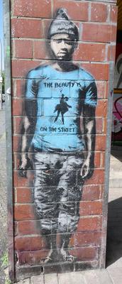 Man in blue t-shirt and black beanie. On shirt is the text: The beauty is on the street
