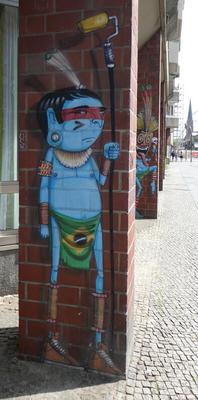 Blue-skinned indigenous person with loincloth made from Brazilian flag. He is carrying a paint roller and has a bored expression.