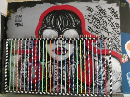 Woman in goggles. Painting is behind a fence with multi-coloured candy-striped rods.