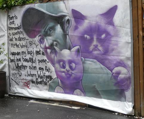 Green-tinted man holding a smiling purple kitten. Behind him, an angry-looking purple cat.