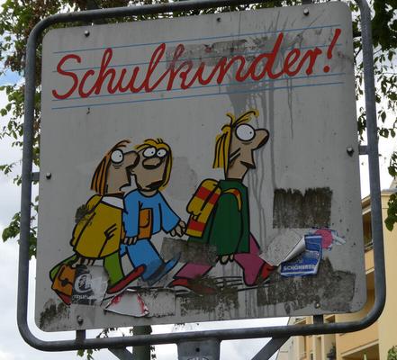 Cartoon children carrying books and backpacks, walking across a street. Text in script font: Schulkinder!