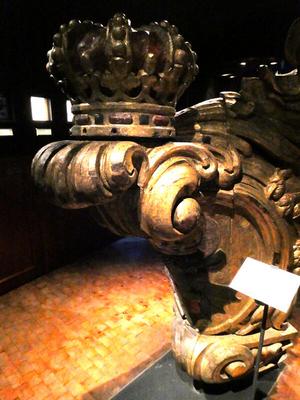 Front part of a wooden sailing vessel, ornately carved and with a crown on top