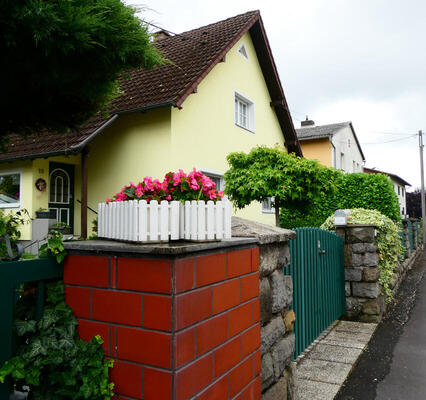 Light yellow house with white wooden planter and pink flowers in front