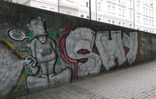 Man holding spray paint can next to large word SHY.