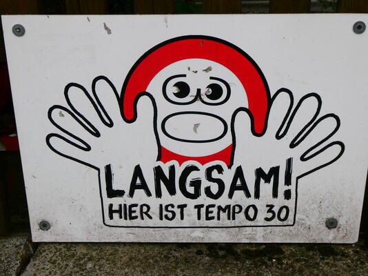 Cartoon speed limt symbol with anxious expression holding up hands: Langsam! Hier ist Tempo 30