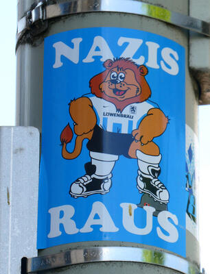 Lion in football uniform with foot on Nazi helmet. Text: Nazis raus