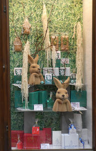 Display case at a chocolate shop. On shelves are rabbits with their paws folded under their chins.