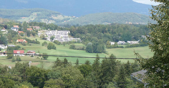 Trees in foreground, modern apartment complex in midground, mountains in background