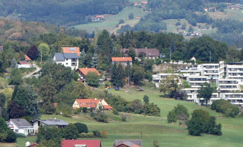 Houses and trees at left, modern apartment complex at right. Hill with trees on it in background