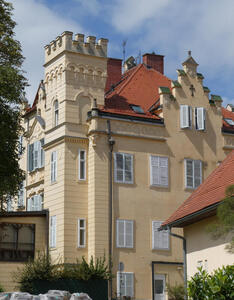 Yellow multi-story building with brick castle-like tower at corner and red roof.