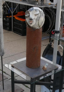 Spherical picasso-style head of a woman on a rust-colored metal cylinder.