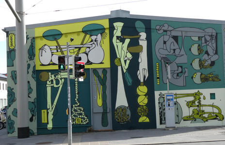 Abstract shapes in dark green and yellow. One is identifiable as a slingshot.