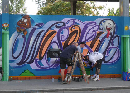 Artists at work on a portion of the wall; they are standing around a ladder.