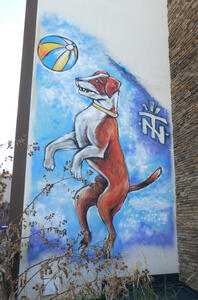 Brown and white dog on its hind legs, playing with a blue and yellow striped ball in the air