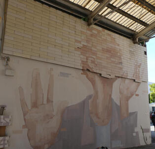 Person looking upwards, hands upraised. The top half of the wall is brickwork, so the painting has a mosaic effect.