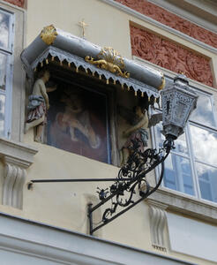 Decorative awning over a painting. Holding up the awning, two statues. Under the awning area, a street lamp projects from the wall.