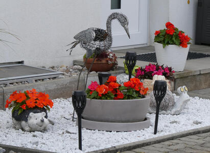 Flowers in planters shaped like a hedgehog and a snail. Behind them, a metal swan