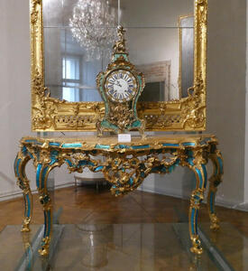 Ornate desk clock on table; behind it, a gold-framed mirror.