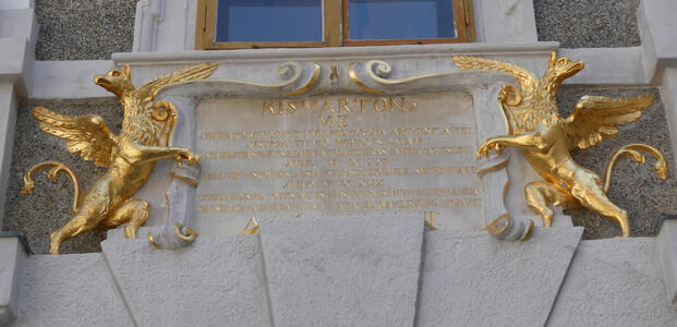 Two gold griffins flanking a plaque with gold inscription.