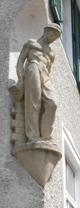 Small sculpture of workman. Behind him is a stack of bricks.