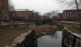 View along path of creek, with brick walls on right and bushes on left.