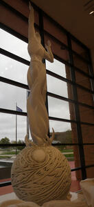 Man standing on sphere, one arm upraised.