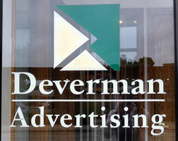 Sign for Deverman Advertising in clean serif font, with a rectangle logo made up of three triangles