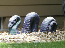 Stone sculpture of a sea serpent that makes it look as if it is swimming through a bed of small rocks.